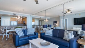 Ein geräumiges Wohnzimmer mit blauen Sofas, einem Couchtisch und einem Essbereich mit weißen Stühlen.