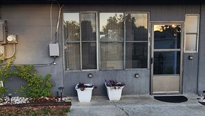 Een gebouw met een grijze gevel, grote ramen en twee witte plantenbakken met beplanting.