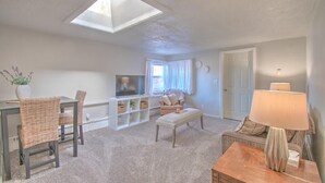 Ein Wohnzimmer mit hoher Decke, einem Fernseher, einer Couch, einem Esstisch mit Stühlen und einer Lampe.