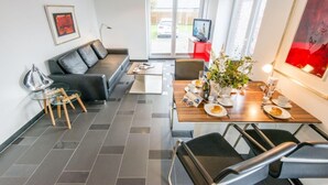 Een moderne woonkamer met een bank, een eettafel gedekt voor twee personen en een televisie op de achtergrond.