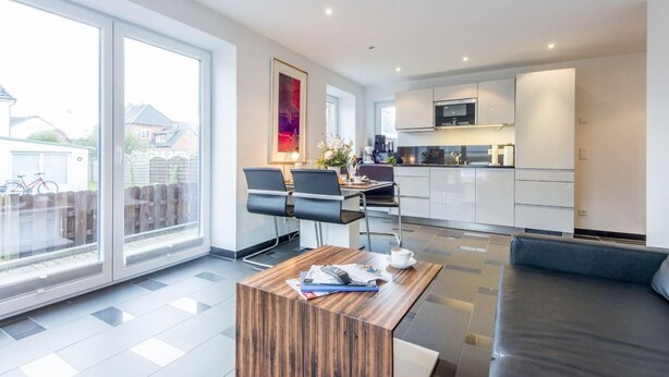 Een moderne keuken met witte kastjes, een magnetron, en een eethoek met een houten tafel en stoelen.