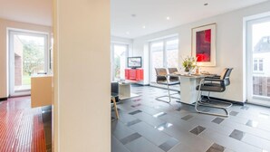 Een moderne hotelkamer met een groot raam, een zithoek met een tafel en stoelen, en een televisie op een standaard.