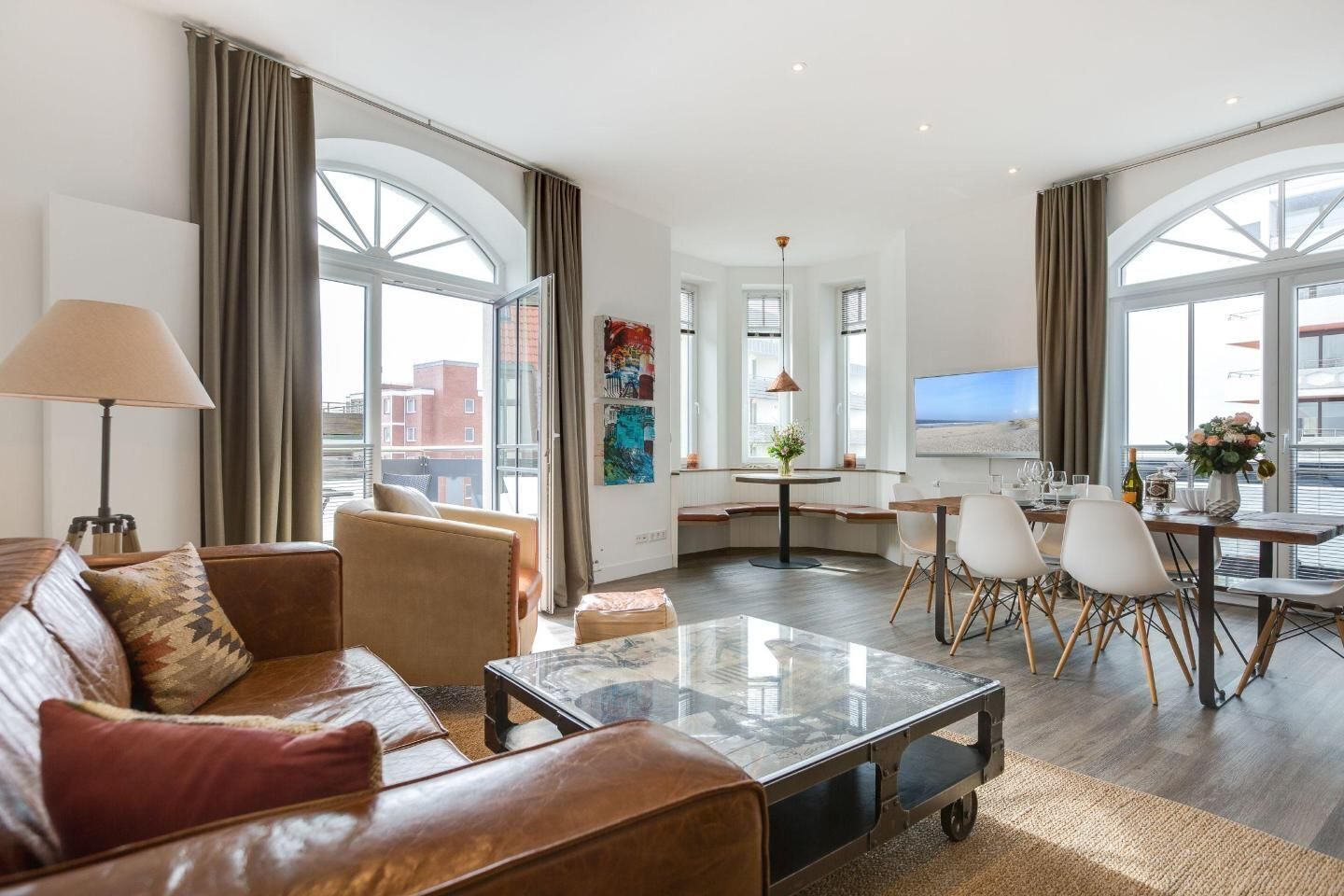A modern hotel room with a living area, dining space, and large windows offering city views.