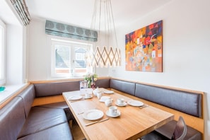 Un comedor moderno con una mesa de madera dispuesta para cuatro, asientos acolchados grises y un cuadro abstracto y colorido en la pared.