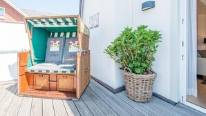 Une terrasse en bois avec une chaise de plage en osier et une plante en pot.