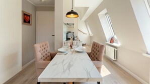 Un comedor con una mesa de mármol, dos sillas tapizadas, una lámpara colgante y una cocina al fondo.