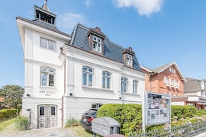 Un bâtiment historique appelé « Die Villa 1903 », doté d’un style architectural classique, avec une entrée imposante et une voiture garée devant.