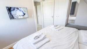 A hotel room with a bed, white linens, a folded towel, a painting of a wolf, and a door leading to another room. - Komfortabel. Ruhig. Gemütlich. - Ringhoog Hüs Whg. 3 "wiesenblick" - Objekt-id: Rhh/03 - Ringhoog (Sylt)