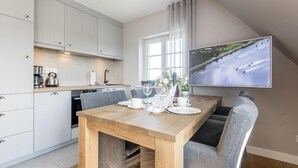 A modern kitchen with white cabinets, a wooden dining table set with white plates, glasses, and cutlery. - Komfortabel. Ruhig. Gemütlich. - Ringhoog Hüs Whg. 3 "wiesenblick" - Objekt-id: Rhh/03 - Ringhoog (Sylt)