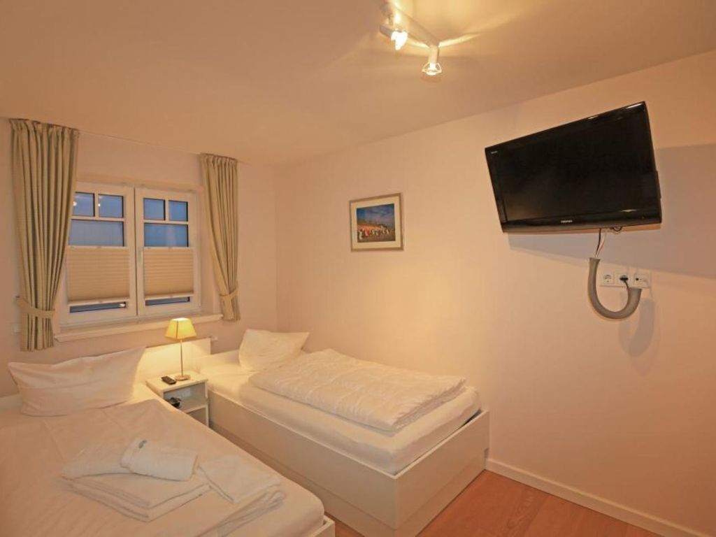 Una habitación de hotel con dos camas, un televisor montado en la pared y una ventana con cortinas.