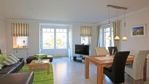 Un salon comprenant un canapé, une table basse, un téléviseur et un coin repas avec des chaises et une table.