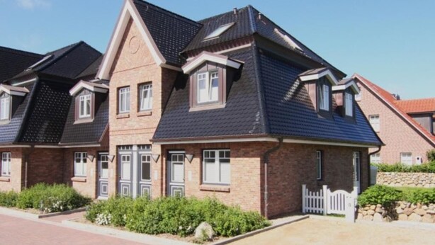Une maison moderne à deux étages, avec une façade en briques, de nombreuses fenêtres et un toit en pente.