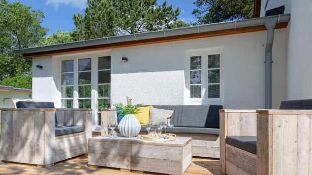 A modern outdoor seating area with wooden furniture and a white wall. - House Mühlenweg, Germany (Sylt)