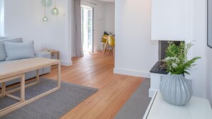 A modern living room with a sofa, a dining table, and a kitchen area visible through an open door. - House Mühlenweg, Germany (Sylt)