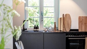 A modern kitchen with a central island, a double oven, and a window with a view of greenery. - House Mühlenweg, Germany (Sylt)