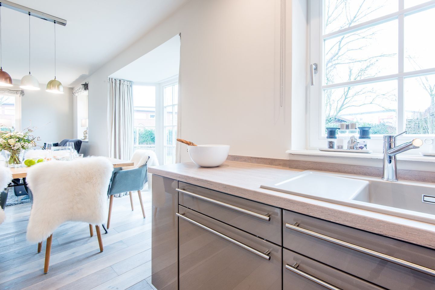 A modern kitchen with a large window, stainless steel appliances, and a dining area with a white chair and table.