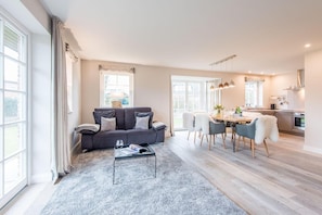 A modern living room with a grey sofa, a coffee table, and a dining area with chairs and a table. - Großzügig. Sauna. Schick. - Hues Lina - Objekt-id: Htt/03 - Haus Alte Dorfstraße (Sylt)