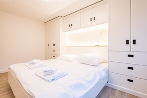 A neatly made bed with white linens and towels, a bedside table, and a wardrobe with multiple compartments.