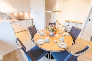 A modern kitchen with white cabinets, a wooden dining table set for four, and a vase of flowers.