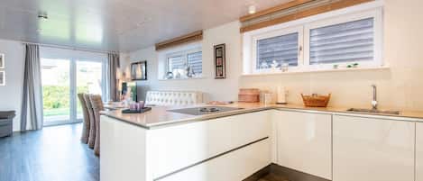 Una cocina moderna con una isla central, muebles blancos y un ventanal con persianas.