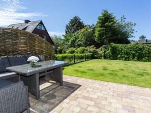 A patio with wicker furniture, a table with a vase, and a brick pathway. - Haus Waldwinkel 18, Whg. Auszeit - Exklusiv. Strandnah. Auszeit. - Haus Waldwinkel 18, Whg (Sylt)