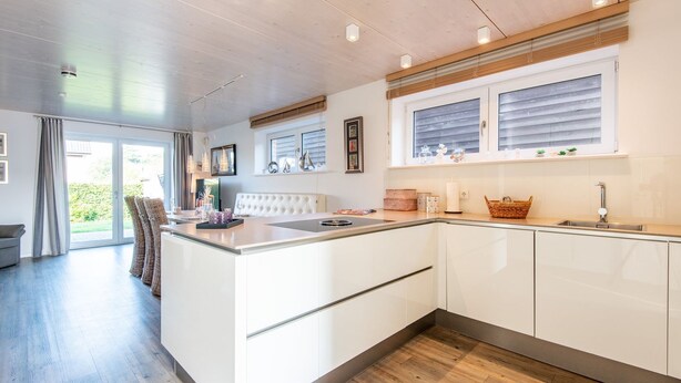Una cocina moderna con una isla central, muebles blancos y un ventanal con persianas.