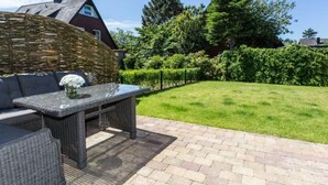 Une terrasse dotée de meubles en osier, une table ornée d’un vase et un chemin en briques.