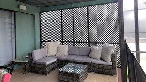 A balcony with a wicker sofa, cushions, and a glass coffee table. - Grand Oak Resort Waterfront Pool/Spa/2 King BR/kayak/Pet extended stay discounts (Apollo Beach)