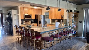 Una cocina moderna con armarios de madera, una isla central con taburetes de bar, electrodomésticos de acero inoxidable e iluminación colgante.
