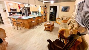 A modern kitchen with a central island, wooden bar stools, a sofa with cushions, and a dining area. - Grand Oak Resort Waterfront Pool/Spa/2 King BR/kayak/Pet extended stay discounts (Apollo Beach)