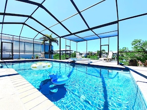 A swimming pool with clear blue water, surrounded by a covered area with lounge chairs.