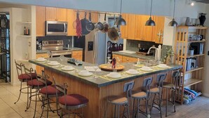 A spacious kitchen with a large island, bar stools, hanging pots, and a modern ceiling design. - Grand Oak Resort Waterfront Pool/Spa/2 King BR/kayak/Pet extended stay discounts (Apollo Beach)