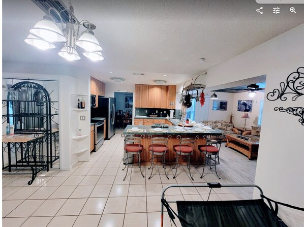 A spacious kitchen with a central island, wooden cabinets, and a dining area with red chairs.