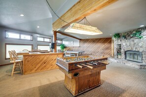 A cozy room with a wooden foosball table, a stone fireplace, and a dining area with chairs and a table. - Silverthorne Condo: New Pool & Hot Tub + Fireplace (Silverthorne)