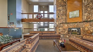 A spacious living area with a stone fireplace, a high ceiling, and a balcony with a railing. - Silverthorne Condo: New Pool & Hot Tub + Fireplace (Silverthorne)