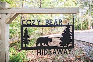 Une enseigne en bois portant l’inscription « COZY BEAR HIDEAWAY » et représentant en silhouette un ours et des arbres.