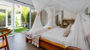 A bedroom with a wooden bed, white bedding, and a canopy. There is a sliding glass door leading to a garden with potted plants.