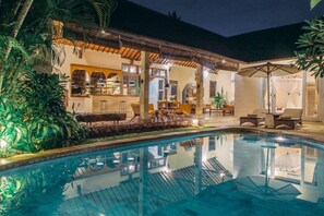 Un espace aménagé au bord de la piscine, avec une piscine à eau claire, des sièges extérieurs et un patio couvert.