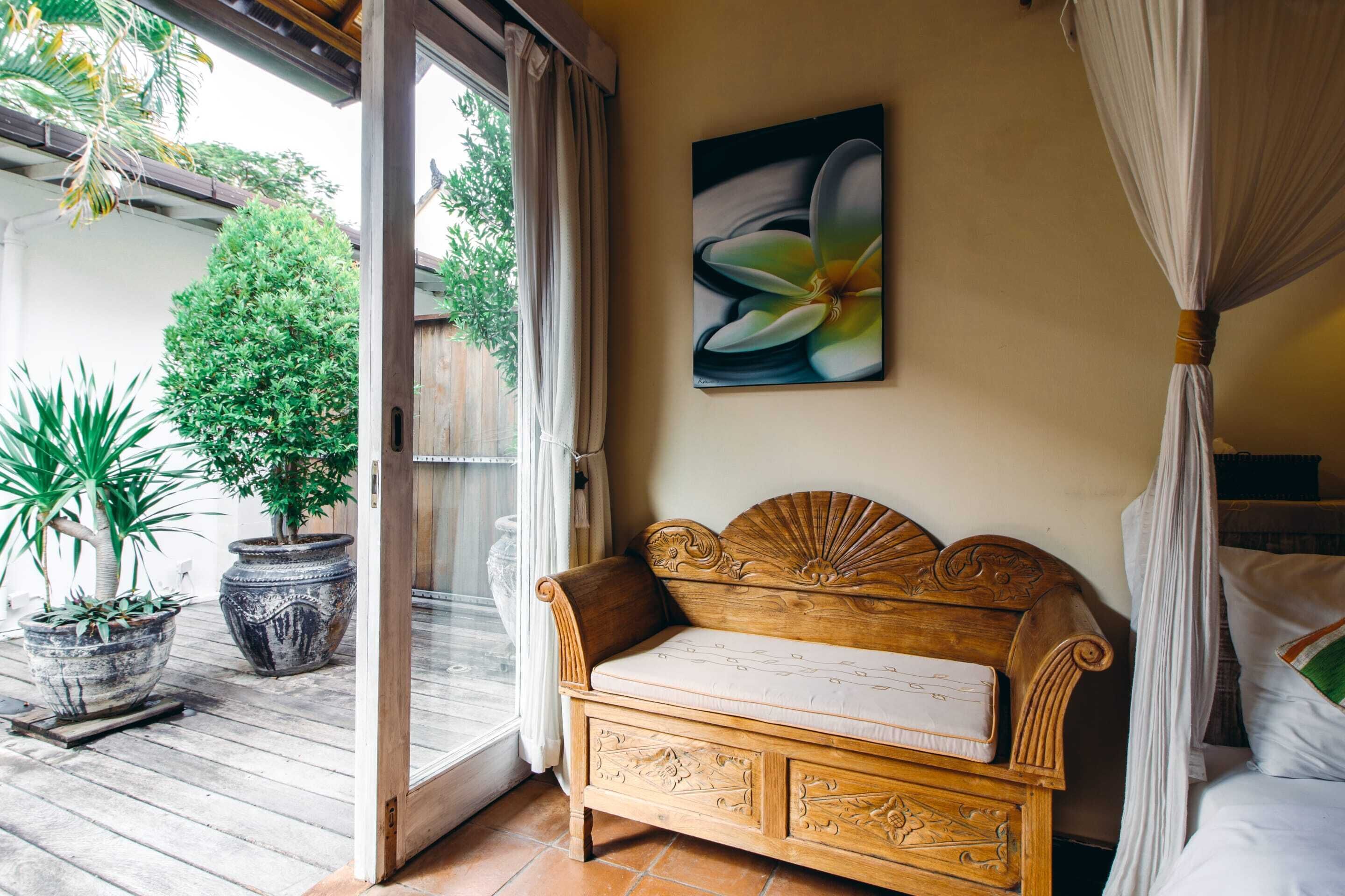 A room with a wooden bench, a bed with a canopy, and a large window with curtains.