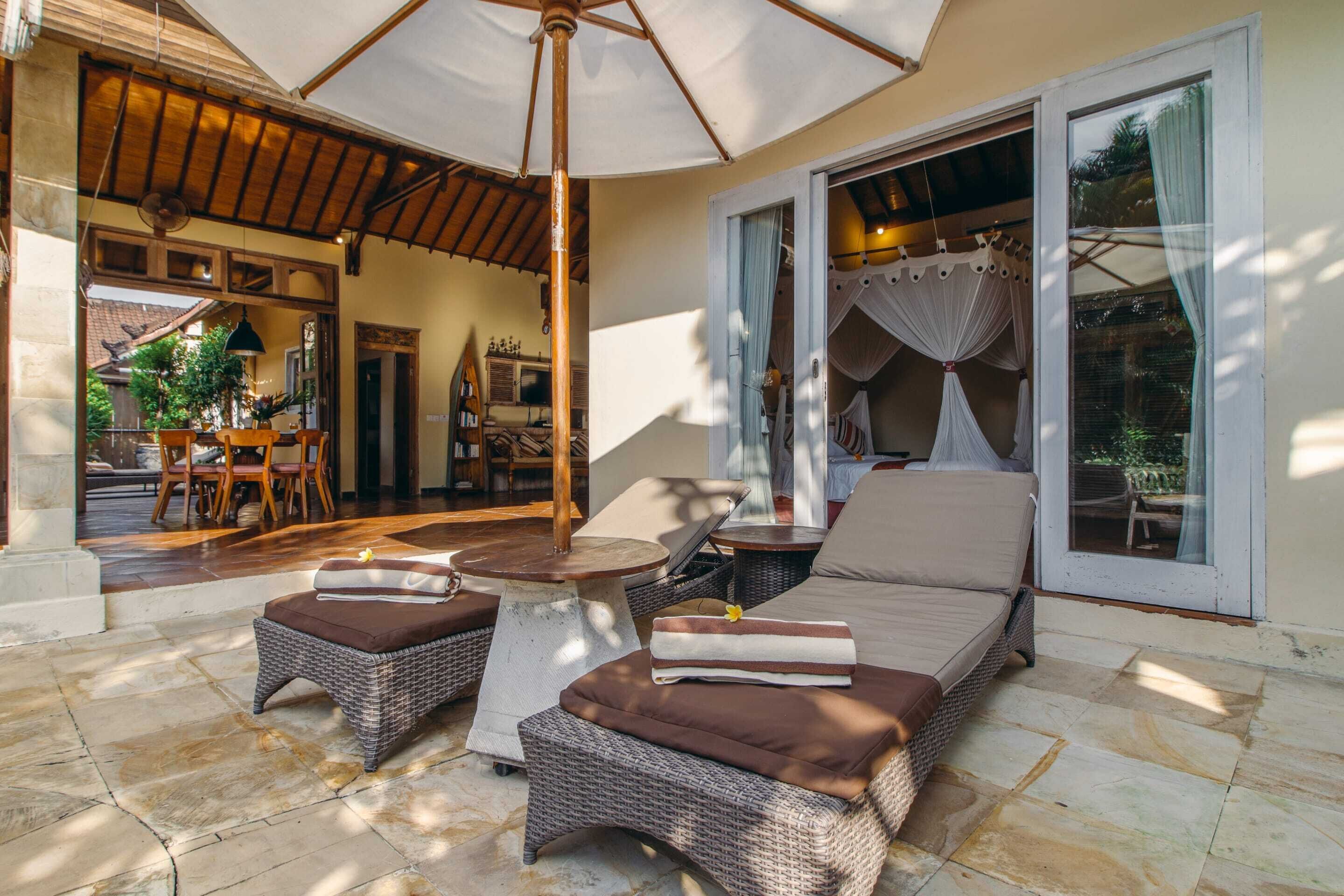 Een zonnig terras met rieten meubels, een ventilator en een grote parasol.