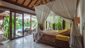 Un dormitorio amplio con una cama grande, dosel y vista a una piscina y exuberante follaje.