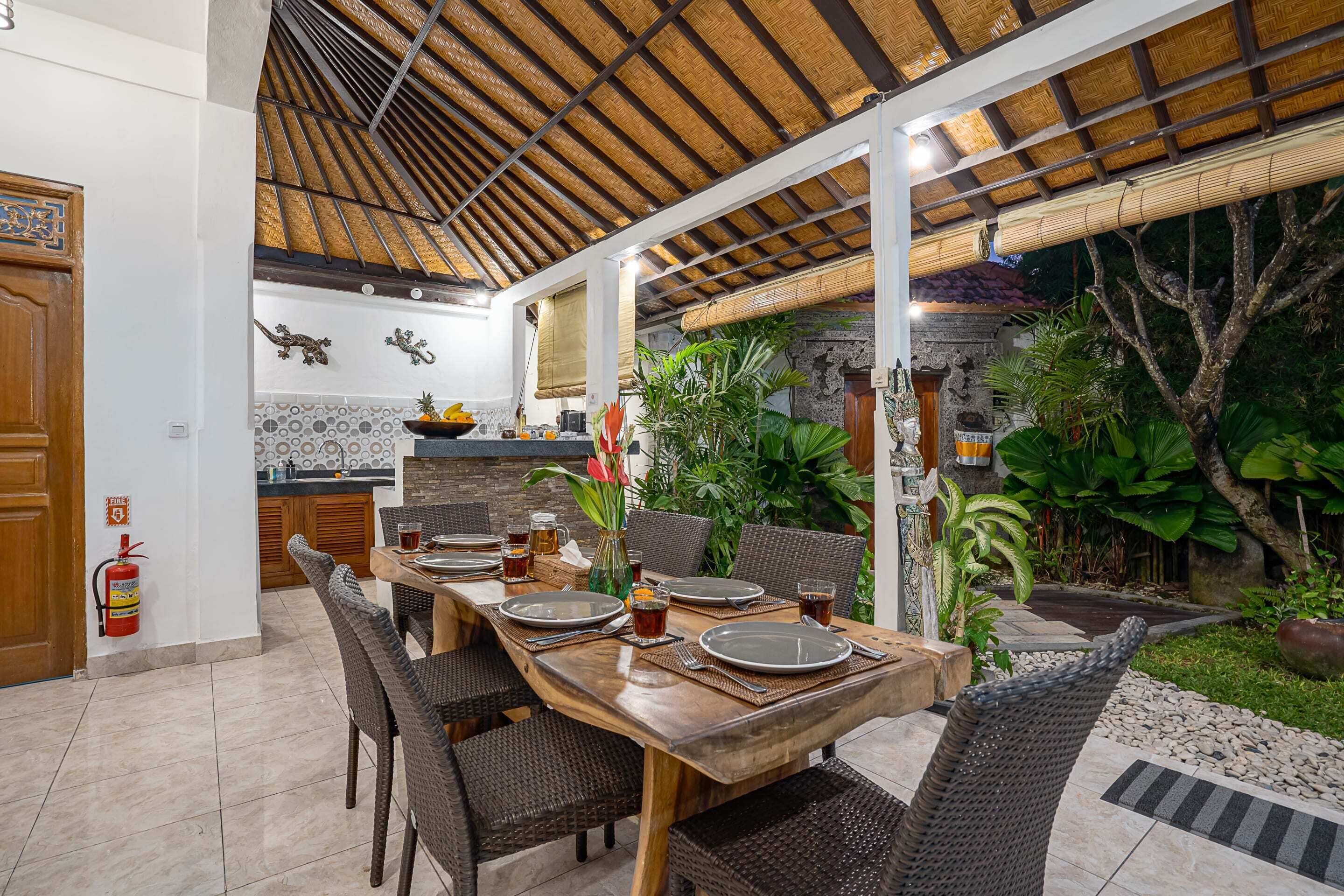 Un área de comedor al aire libre con una mesa de madera dispuesta para cuatro personas, rodeada de sillas de mimbre.