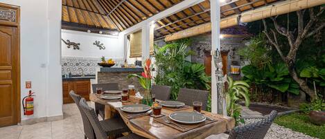 An outdoor dining area with a wooden table set for four, surrounded by wicker chairs.