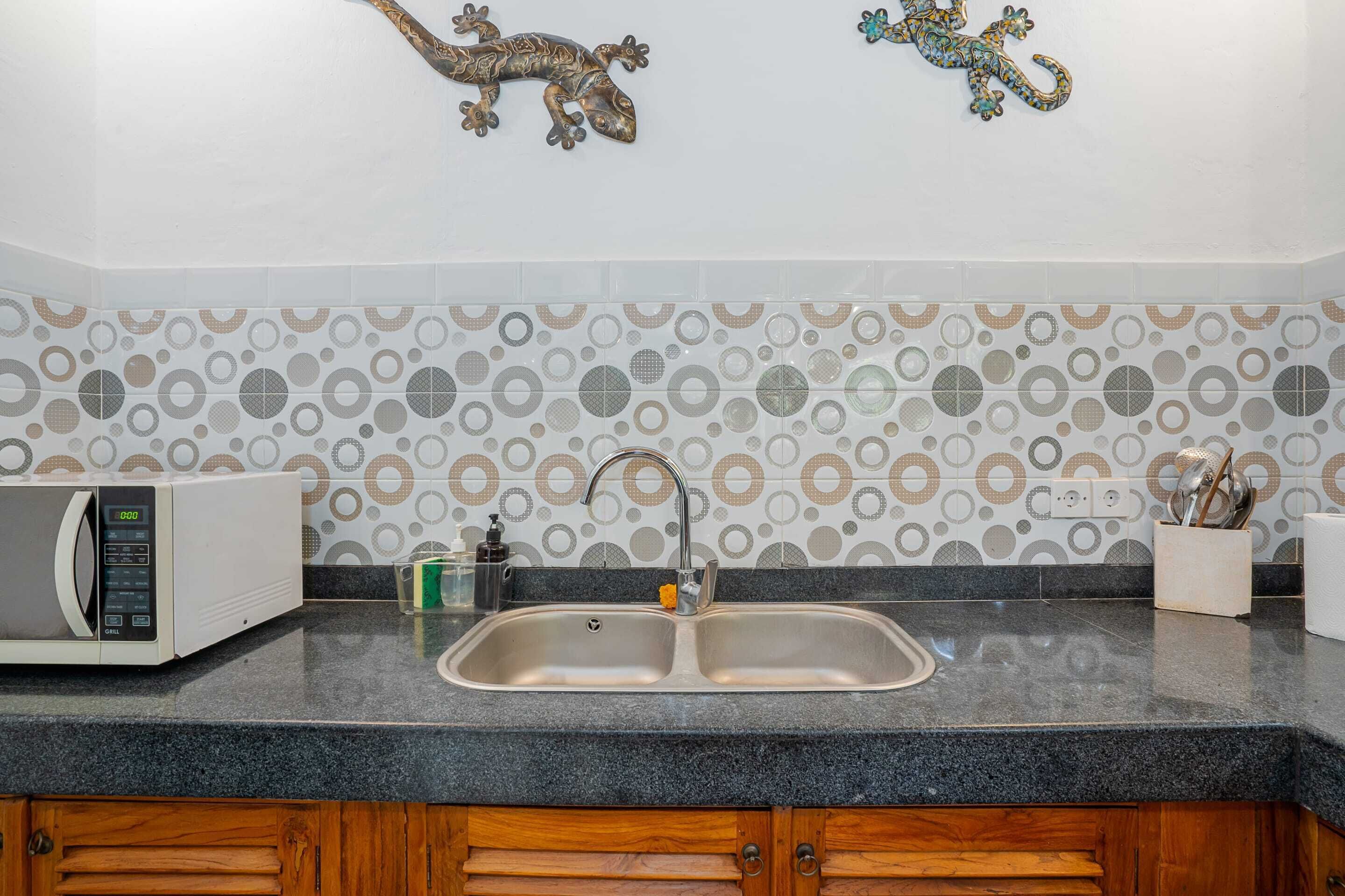 A kitchen with a double sink, a microwave, and decorative wall tiles.