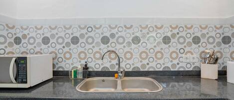 A kitchen with a double sink, a microwave, and decorative wall tiles.