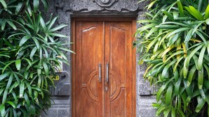 A wooden double door with a stone wall and tropical plants on either side. - Villa Shanti (Seminyak)