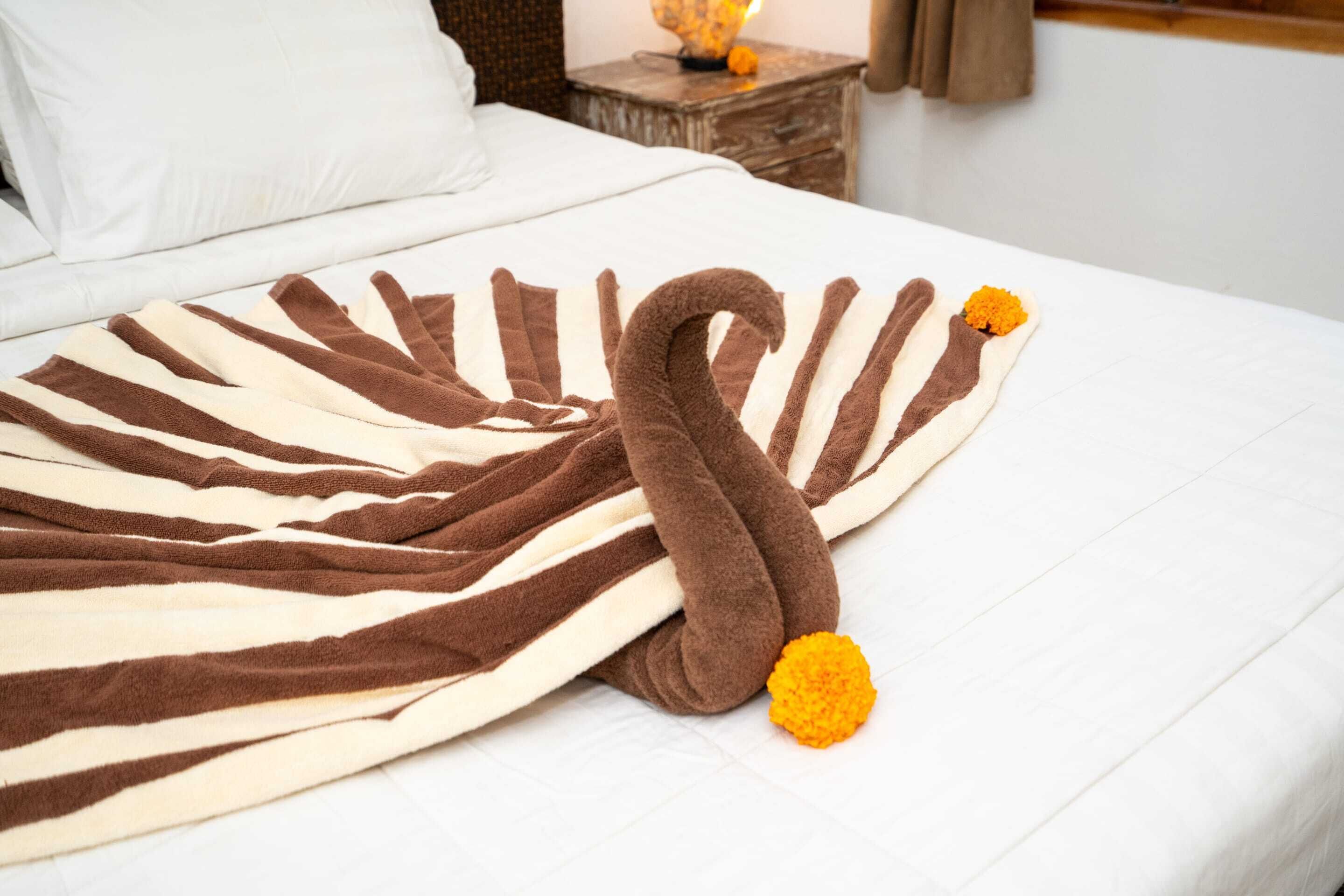 Un letto con coperta a righe e una decorazione a testa di cigno con fiori arancioni.