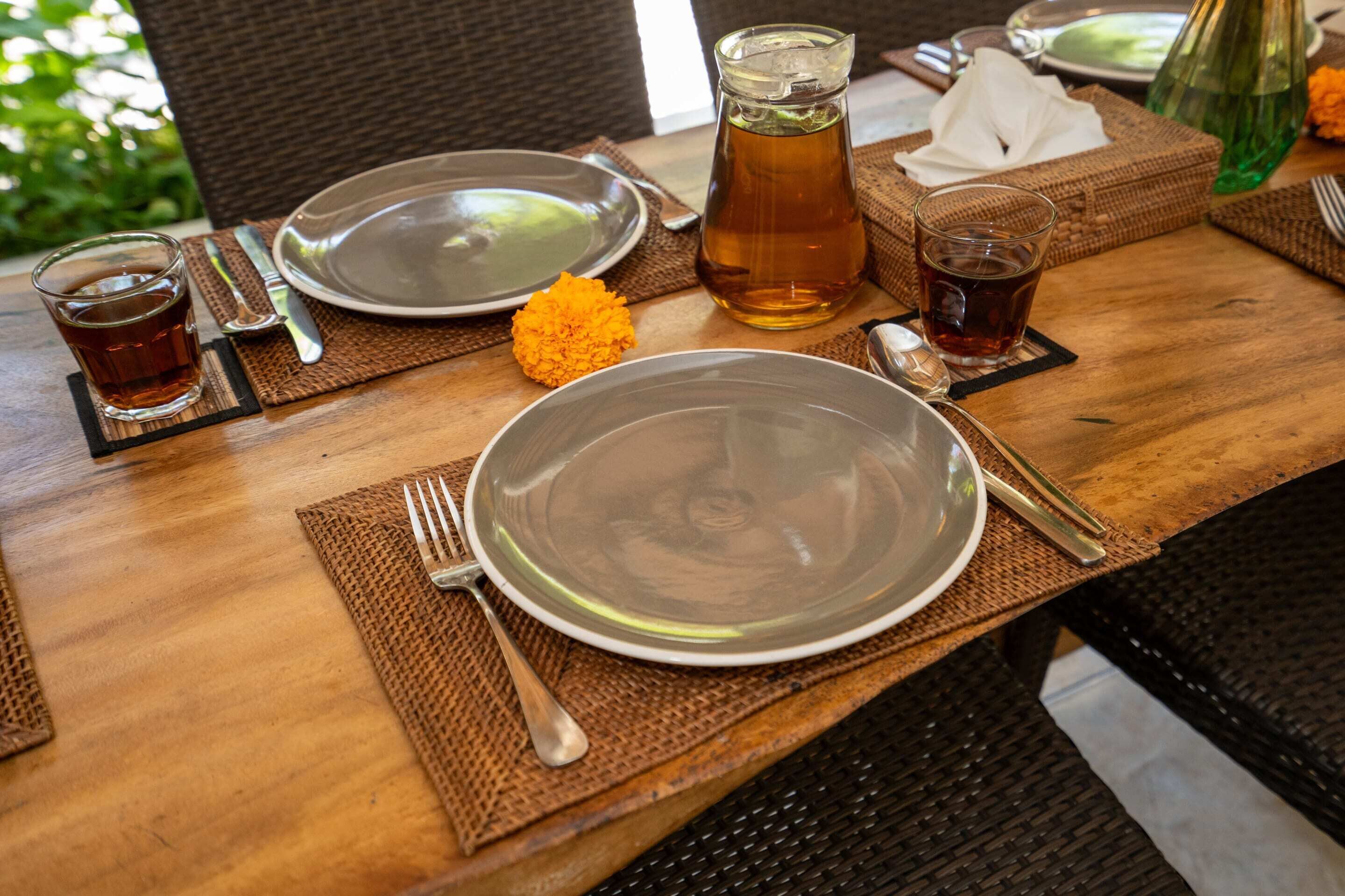 Una mesa de comedor dispuesta con platos, cubiertos, una jofaina de té y un vaso de agua.