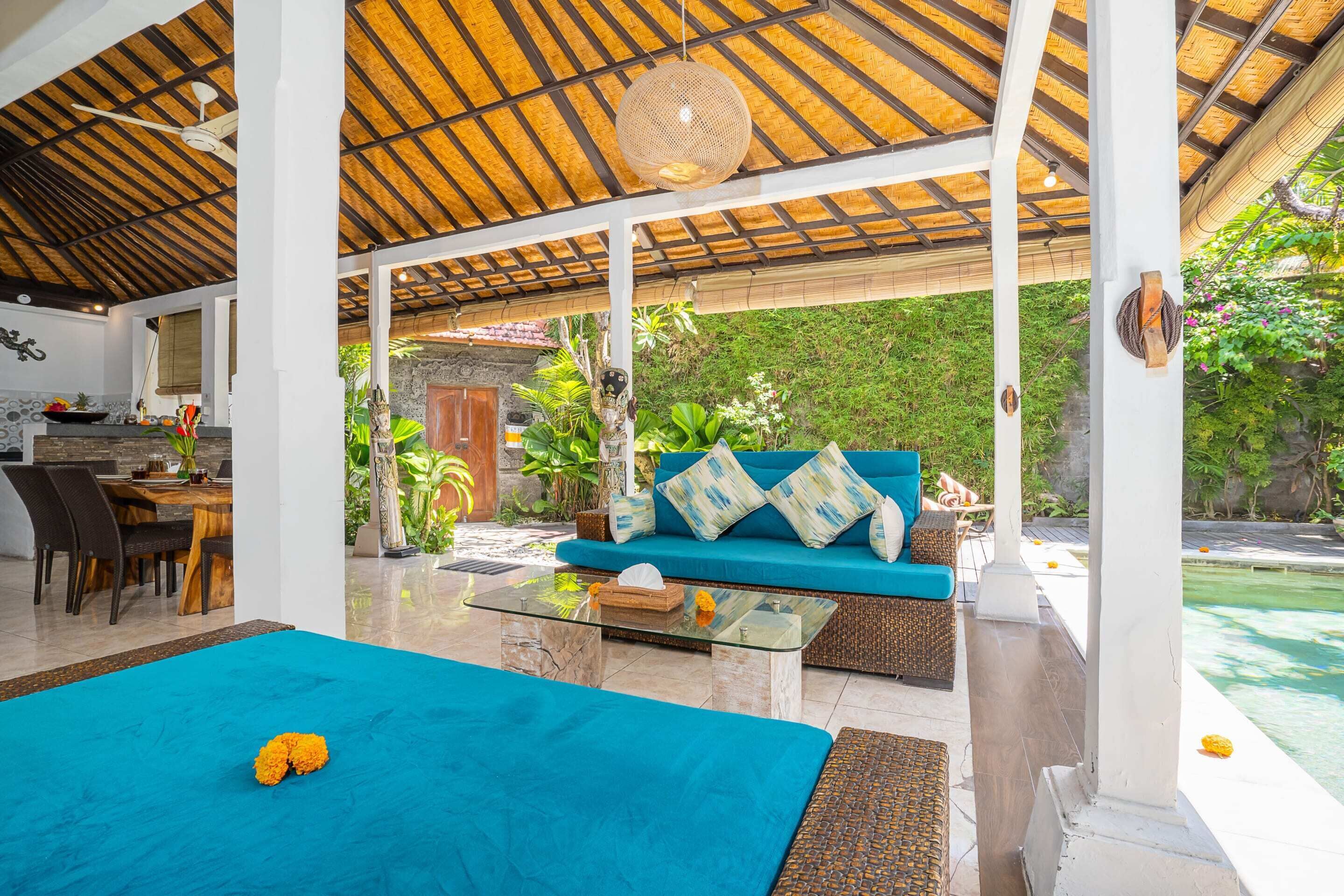 A covered outdoor seating area with a sofa and a glass coffee table, surrounded by lush greenery.