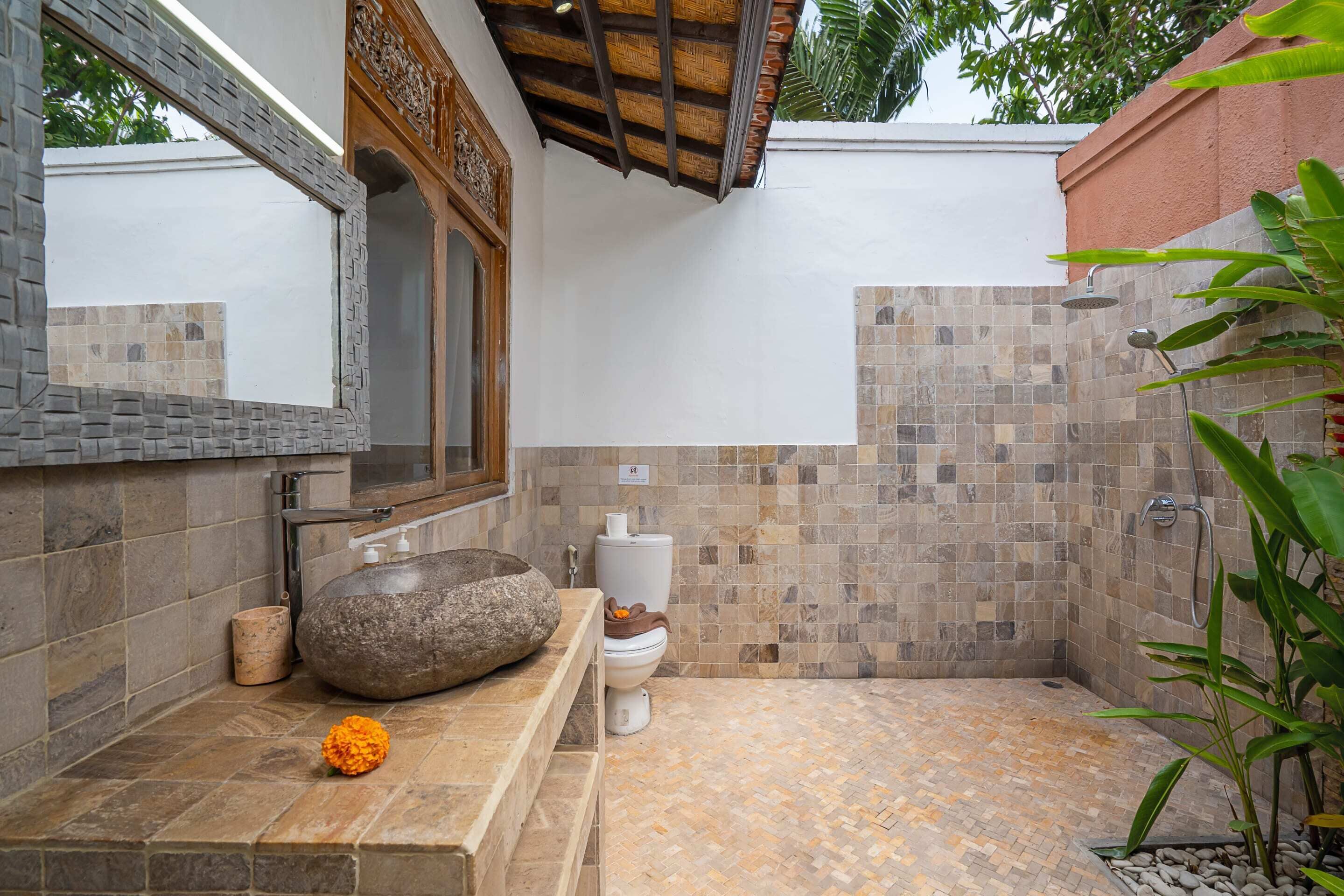 A bathroom with a stone sink, a toilet, and a shower area with mosaic tiles.